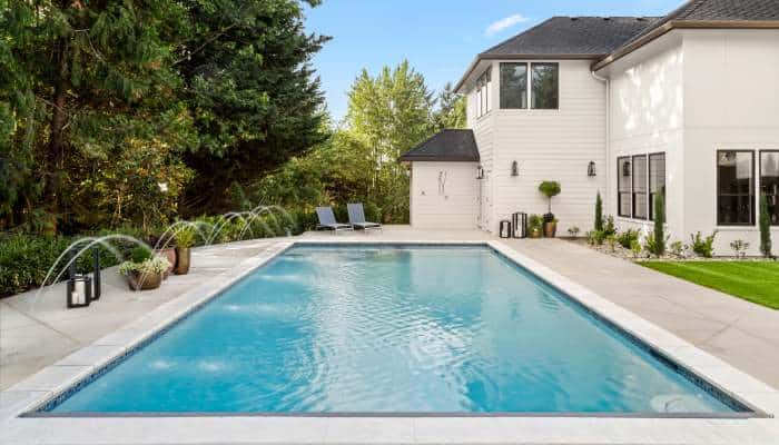The exterior of a white multi-story house with a rectangular pool and mature landscaping in the backyard.