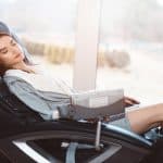 A woman is resting in a black massage chair that sits next to a sliding glass door. She has her eyes closed.