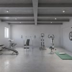 A landscape view of a basement home gym with concrete floors, grey walls, and various workout equipment.