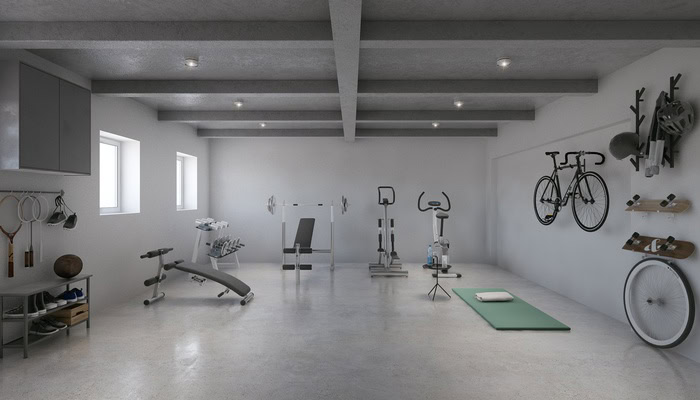 A landscape view of a basement home gym with concrete floors, grey walls, and various workout equipment.