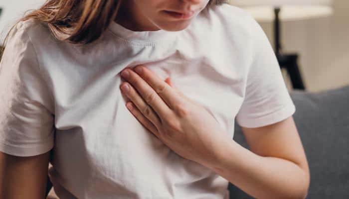 A young woman wearing a simple white t-shirt holding her hand to her chest, her face cast downward.