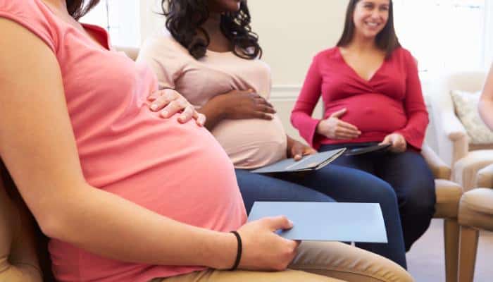 A group of pregnant women sitting in chairs in a circle. Each woman has a hand on her belly and a pamphlet in hand.