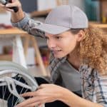 A woman looking at a wheelchair to inspect it and ensure it is safe. She is wearing casual clothes and a hat.