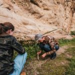 A mature woman and a young adult inspecting the ground of a trail while wearing camouflage and exploring outdoors.