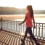 A young, active woman wears activewear and a ponytail as she takes a walk across a bridge at sunset.
