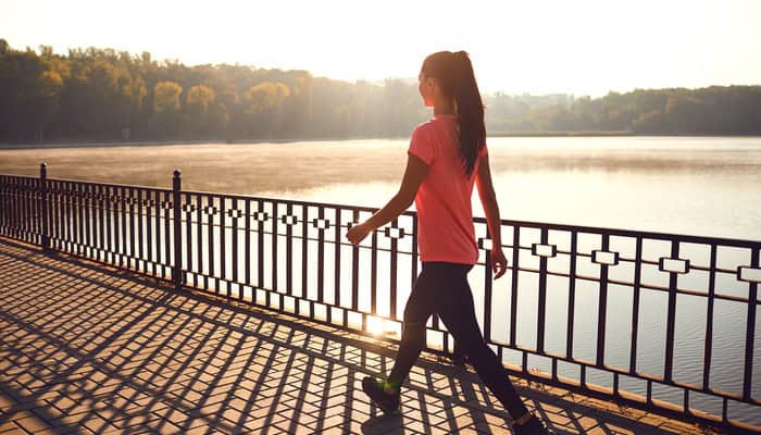 A young, active woman wears activewear and a ponytail as she takes a walk across a bridge at sunset.
