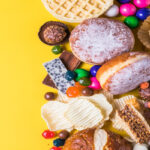 A vibrant flat lay of assorted snacks, including pastries, candies, chips, and chocolates, on a bright yellow background.