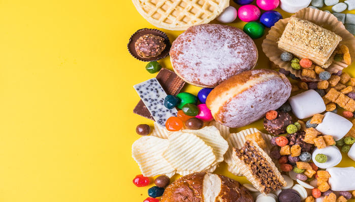 A vibrant flat lay of assorted snacks, including pastries, candies, chips, and chocolates, on a bright yellow background.